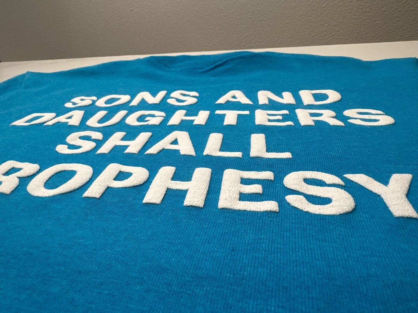 Close-up of a bold white screen print on a turquoise shirt